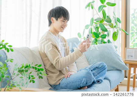 一個男人在客廳看著他的智慧型手機 142261776