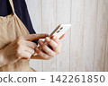 A woman in an apron operating a smartphone 142261850