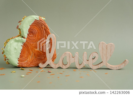 Wooden word LOVE symbol Delicious fresh croissant topped with Matcha Green Tea flavor Ganache. Creation unique heart shape bakery. Puff pastry holiday love gift present idea Valentine's day 142263006