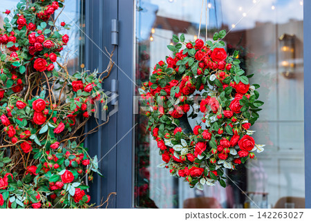 a festive red rose wreath hanging on a doorway with green leaves and twine, creating a warm holiday decoration for home decor a festive red rose wreath hanging on a doorway with green leaves and twine, creating a warm holiday decoration for home decor 142263027