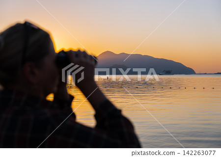 Defocused Woman Looking Through Binoculars on Marmaris Waterfront at Golden Hour Defocused Woman Looking Through Binoculars on Marmaris Waterfront at Golden Hour 142263077
