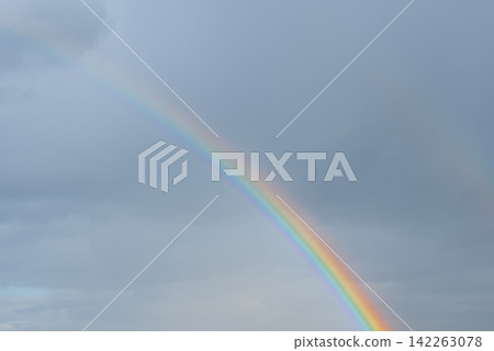 Colorful Rainbow Across Blue Cloudy Sky After Rain. Vibrant rainbow stretches across blue sky filled with soft clouds after rainfall. The colorful atmospheric phenomenon creates striking natural scene Colorful Rainbow Across Blue Cloudy Sky After Rain. Vibrant rainbow stretches across blue sky filled with soft clouds after rainfall. The colorful atmospheric phenomenon creates striking natural scene 142263078