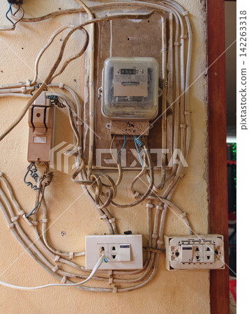 Old electric watt-hour meter and unsafe messy wiring cables on a wall. Old electric watt-hour meter and unsafe messy wiring cables on a wall. 142263318
