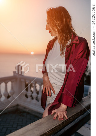 Woman sunset balcony Woman in maroon shirt standing on a terrace overlooking the sea at dusk with copy space Woman sunset balcony Woman in maroon shirt standing on a terrace overlooking the sea at dusk with copy space 142263568