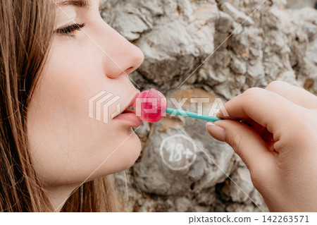 Woman lollipop profile eating a pink sweet candy with eyes closed in front of a rocky stone wall with copy space Woman lollipop profile eating a pink sweet candy with eyes closed in front of a rocky stone wall with copy space 142263571