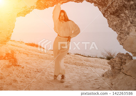 Woman cave sunset posing at the entrance of a coastal cavern during golden hour with a view of the sea Woman cave sunset posing at the entrance of a coastal cavern during golden hour with a view of the sea 142263586