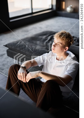 Teen quietly positioned next to window with tranquil expression Teen quietly positioned next to window with tranquil expression 142264450