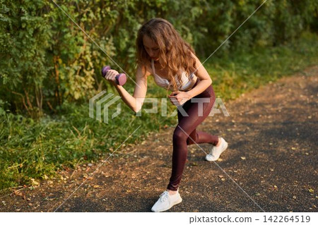 Woman performing precise dumbbell curl in nature setting Woman performing precise dumbbell curl in nature setting 142264519