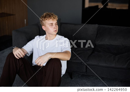 Young individual lounging on sofa gazing at sunset light Young individual lounging on sofa gazing at sunset light 142264950