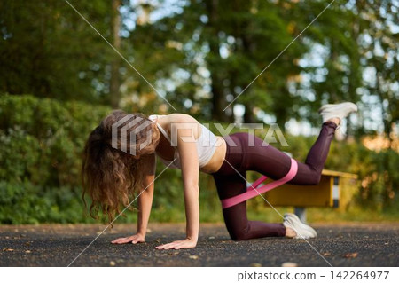 Caucasian woman athlete performing glute pulse in park Caucasian woman athlete performing glute pulse in park 142264977