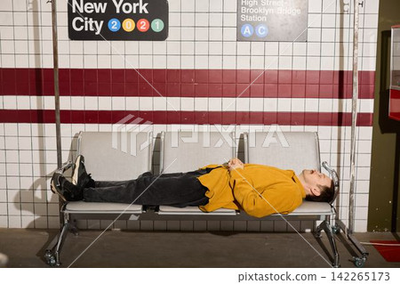 Person dressed in yellow is dozing on subway bench near historic signage Person dressed in yellow is dozing on subway bench near historic signage 142265173