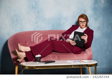 Authority figure sitting confidently on sofa with tablet and pens Authority figure sitting confidently on sofa with tablet and pens 142265344