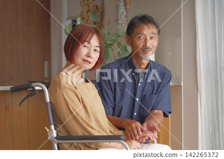 丈夫坐在輪椅上,妻子坐在他旁邊。 丈夫坐在輪椅上,妻子坐在他旁邊。 142265372