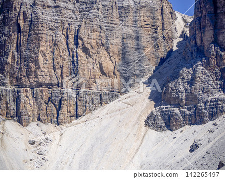 hiking trail to Pordoi massif in the Dolomites rocky cliffs, as seen from the high-altitude green meadows near the famous Viel dal Pan Trail. hiking trail to Pordoi massif in the Dolomites rocky cliffs, as seen from the high-altitude green meadows near the famous Viel dal Pan Trail. 142265497