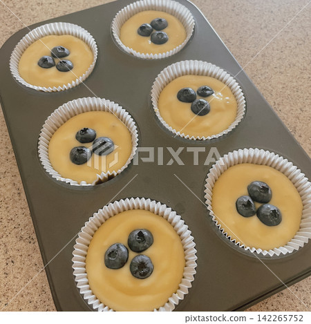 Raw blueberry muffin dough in paper liners inside metal baking pan ready for oven preparation at home kitchen stock photo Raw blueberry muffin dough in paper liners inside metal baking pan ready for oven preparation at home kitchen stock photo 142265752