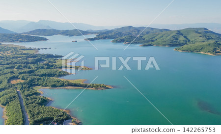 Aerial view of Lake Plastira shoreline with turquoise water, forest hills and distant mountains in Thessaly Greece stock photo Aerial view of Lake Plastira shoreline with turquoise water, forest hills and distant mountains in Thessaly Greece stock photo 142265753