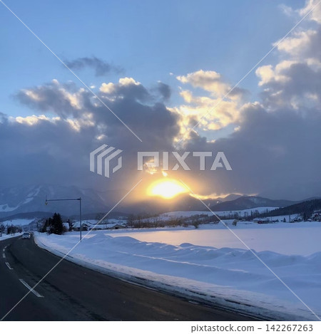 冬日的夕陽照亮了白雪皚皚的平原和山脈,以及一條積雪覆蓋的道路。 冬日的夕陽照亮了白雪皚皚的平原和山脈,以及一條積雪覆蓋的道路。 142267263