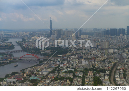 Aerial panoramic view of Ho Chi Minh City showing the Saigon River, a red arch bridge and Landmark 81 skyscraper rising above a vast urban landscape of buildings and neighborhoods. Aerial panoramic view of Ho Chi Minh City showing the Saigon River, a red arch bridge and Landmark 81 skyscraper rising above a vast urban landscape of buildings and neighborhoods. 142267960
