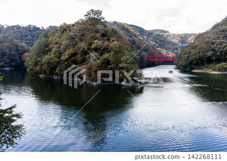 Autumn scenery: a lake and a peninsula dyed in autumn colors, a distant red bridge and pleasure boats, a natural landscape. Autumn scenery: a lake and a peninsula dyed in autumn colors, a distant red bridge and pleasure boats, a natural landscape. 142268111