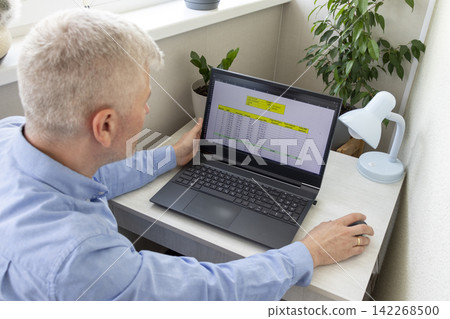 Senior Professional Taking Notes While Analyzing Mortgage Amortization Table on Laptop Screen 142268500