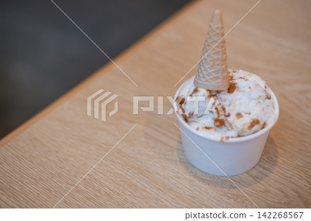 A cup of creamy yogurt ice cream topped with a small miniature ice cream cone 142268567