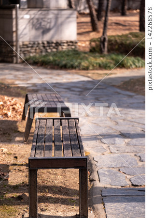 Close up of wooden bench, with stone pathway on the background in public park Close up of wooden bench, with stone pathway on the background in public park 142268578