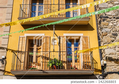 Sunlit yellow house facade with balconies and festive bunting Sunlit yellow house facade with balconies and festive bunting 142268803