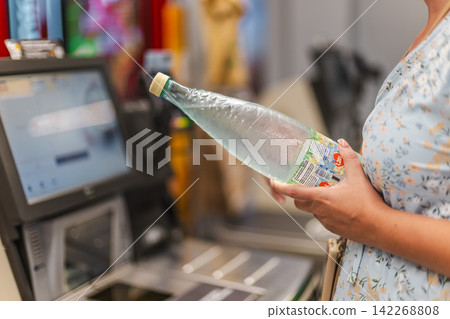 Woman holding plastic bottle at supermarket self-checkout Woman holding plastic bottle at supermarket self-checkout 142268808