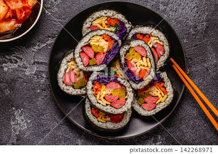 A black plate filled with kimbap (or gimbap) that have colorful fillings. 142268971