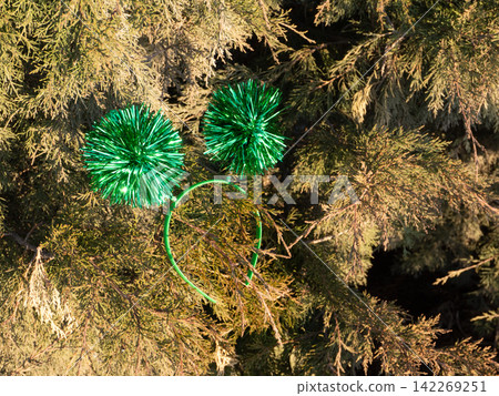 Green tinsel headband with sparkly pom-poms resting on evergreen tree branches. St Patrick's Day party accessory and holiday decoration concept Green tinsel headband with sparkly pom-poms resting on evergreen tree branches. St Patrick's Day party accessory and holiday decoration concept 142269251