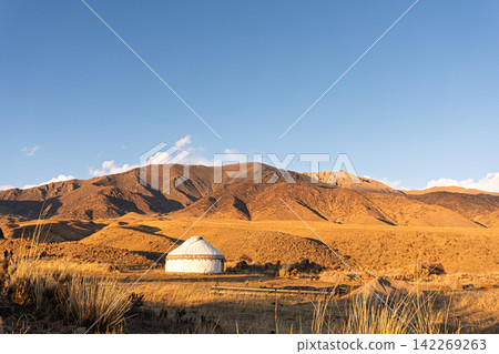 Traditional white yurt in a mountain valley during golden hour. Scenic landscape of a nomadic dwelling in Central Asia(Kyrgyzstan). Copy space 142269263