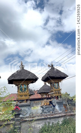 serene balinese temple structures with thatched roofs and paintings in gold and red, stationary outdoor daytime scene, low angle looking up, natural light, clean background, editorial use. serene balinese temple structures with thatched roofs and paintings in gold and red, stationary outdoor daytime scene, low angle looking up, natural light, clean background, editorial use. 142269926