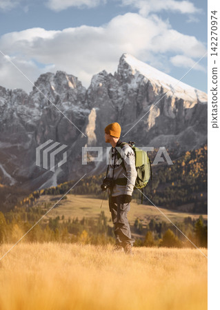Hiker standing in golden grass with the Sassolungo mountain group Hiker standing in golden grass with the Sassolungo mountain group 142270974