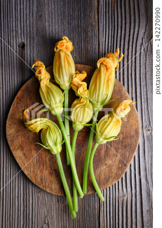 Overhead zucchini blossoms placed on round wooden board Overhead zucchini blossoms placed on round wooden board 142270990