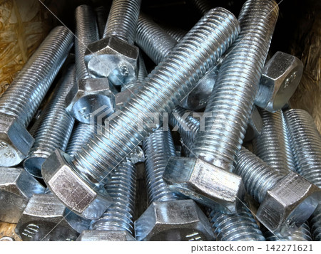 Close up of shiny metallic bolts and nuts piled in a workshop setting Close up of shiny metallic bolts and nuts piled in a workshop setting 142271621