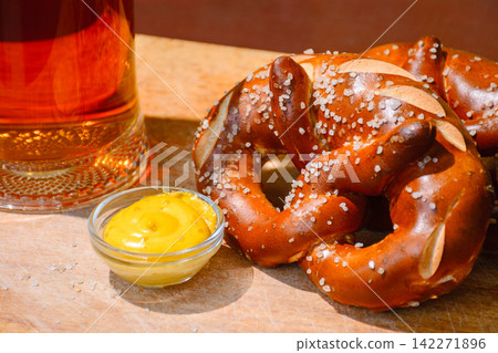beer pretzel and mustard on a wooden table. rustic oktoberfest drink and food background. grungy wall texture. closeup view beer pretzel and mustard on a wooden table. rustic oktoberfest drink and food background. grungy wall texture. closeup view 142271896