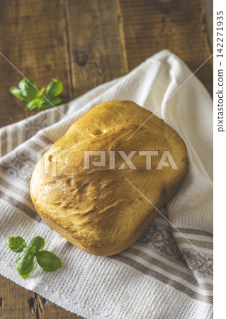 Loaf of freshly baked bread with basil on linen towel over rustic wooden table background. Shallow depth of field. Loaf of freshly baked bread with basil on linen towel over rustic wooden table background. Shallow depth of field. 142271935