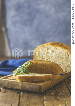 Loaf of freshly baked bread with basil and bread slices on wooden board over rustic wooden table background. Shallow depth of field. Loaf of freshly baked bread with basil and bread slices on wooden board over rustic wooden table background. Shallow depth of field. 142271942