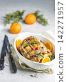 Roasted pork in white dish, christmas baked ham with cranberries, tangerines, thyme, rosemary, garlic on light table surface. 142271957