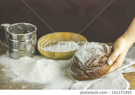 Baker's hands with a bread. Photo with high contrast. Woman hand with rye bread bread on dark wooden table with flour Baker's hands with a bread. Photo with high contrast. Woman hand with rye bread bread on dark wooden table with flour 142271995