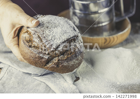 Baker's hands with a bread. Photo with high contrast. Woman hand with rye bread bread on dark wooden table with flour Baker's hands with a bread. Photo with high contrast. Woman hand with rye bread bread on dark wooden table with flour 142271998