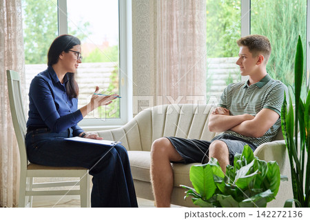 Female psychologist talking to teen boy sitting on sofa in cozy office 142272136