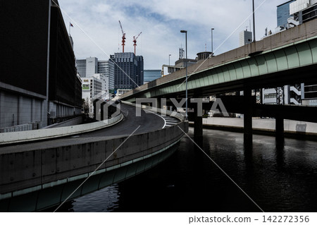 高架鐵路和東京的摩天大樓在深色的水面上投下陰影,這是江戶橋樞紐附近的一幕。 高架鐵路和東京的摩天大樓在深色的水面上投下陰影,這是江戶橋樞紐附近的一幕。 142272356