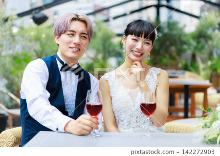 The bride and groom drinking wine on a waterside terrace. The bride and groom drinking wine on a waterside terrace. 142272903