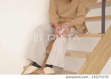 A woman experiences knee pain when going up and down stairs. A woman experiences knee pain when going up and down stairs. 142273170