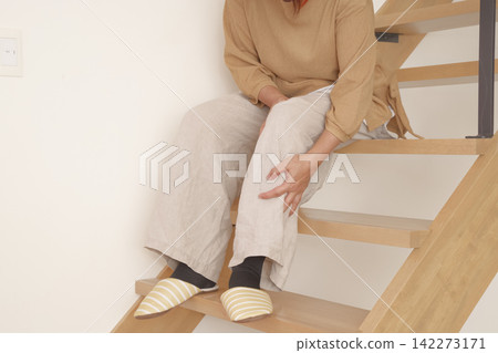 A woman experiences knee pain when going up and down stairs. A woman experiences knee pain when going up and down stairs. 142273171