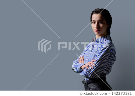 Confident young female student standing with crossed arms looking at camera against studio background Confident young female student standing with crossed arms looking at camera against studio background 142273181
