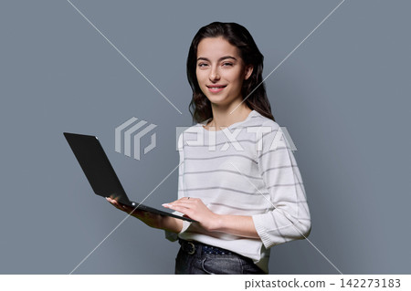 Young female student holding laptop computer and looking at camera on grey background Young female student holding laptop computer and looking at camera on grey background 142273183