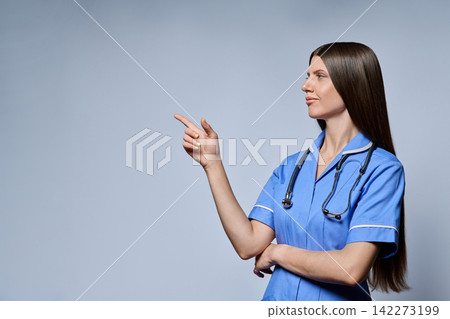 Smiling female nurse pointing finger to side copy space isolated against grey background 142273199