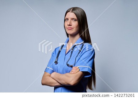 Three-quarter portrait of confident female nurse standing with folded arms on grey background Three-quarter portrait of confident female nurse standing with folded arms on grey background 142273201